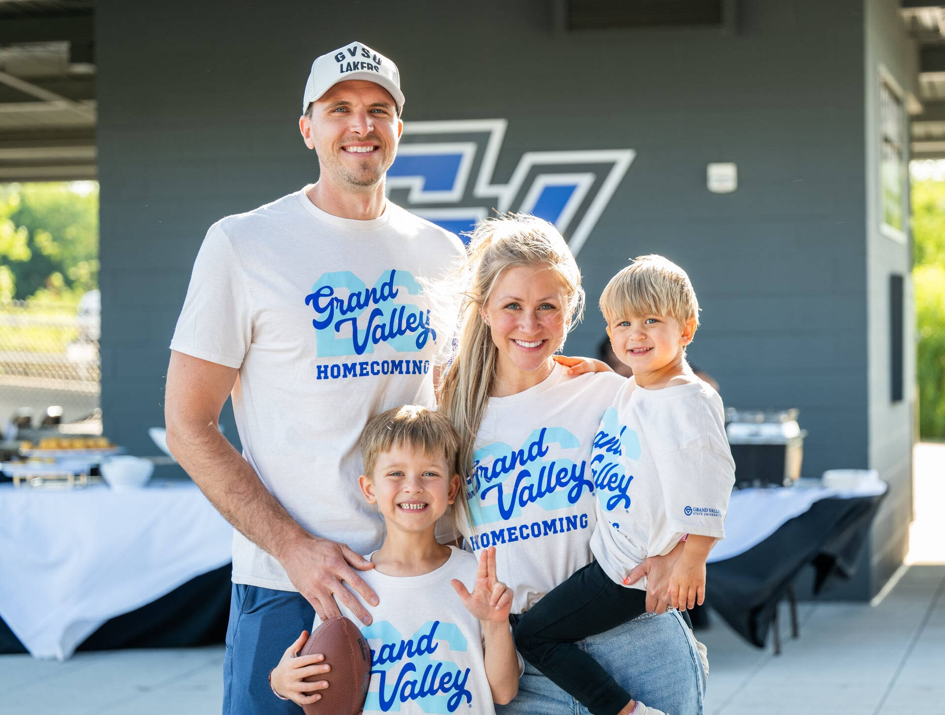 Mike Przydzial stands at left with his wife and two sons, all are dressed in Grand Valley homecoming shirts, script GV over a 26